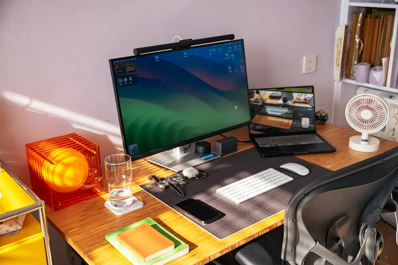 A computer monitor and a laptop on a wooden desk.